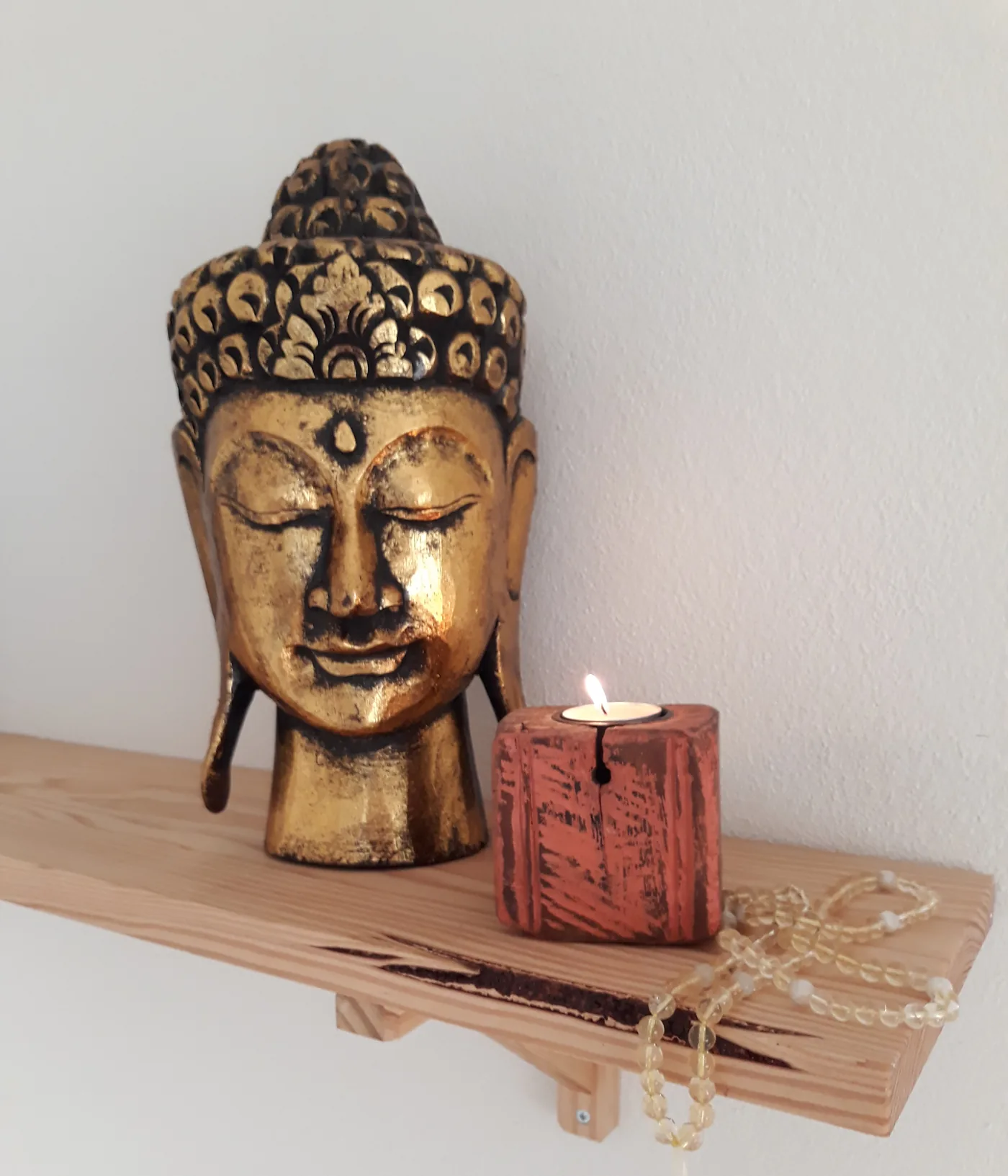 Cabeça de Buda dourada, uma vela acesa e um mala de citrino, na prateleira da sala de yoga.
