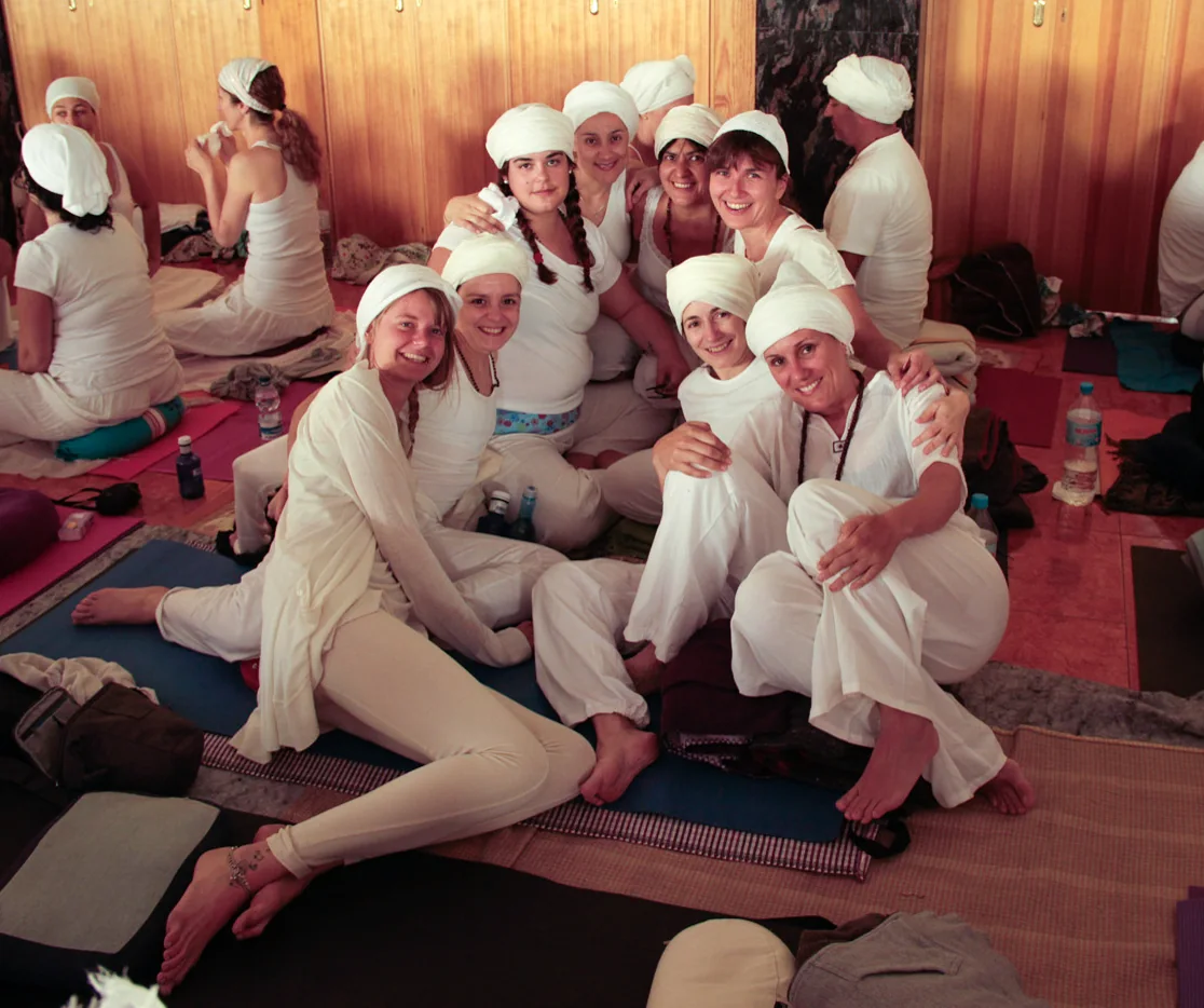 Grupo da formação de Kundalini Yoga, de branco e com turbante, sentado no chão a sorrir.