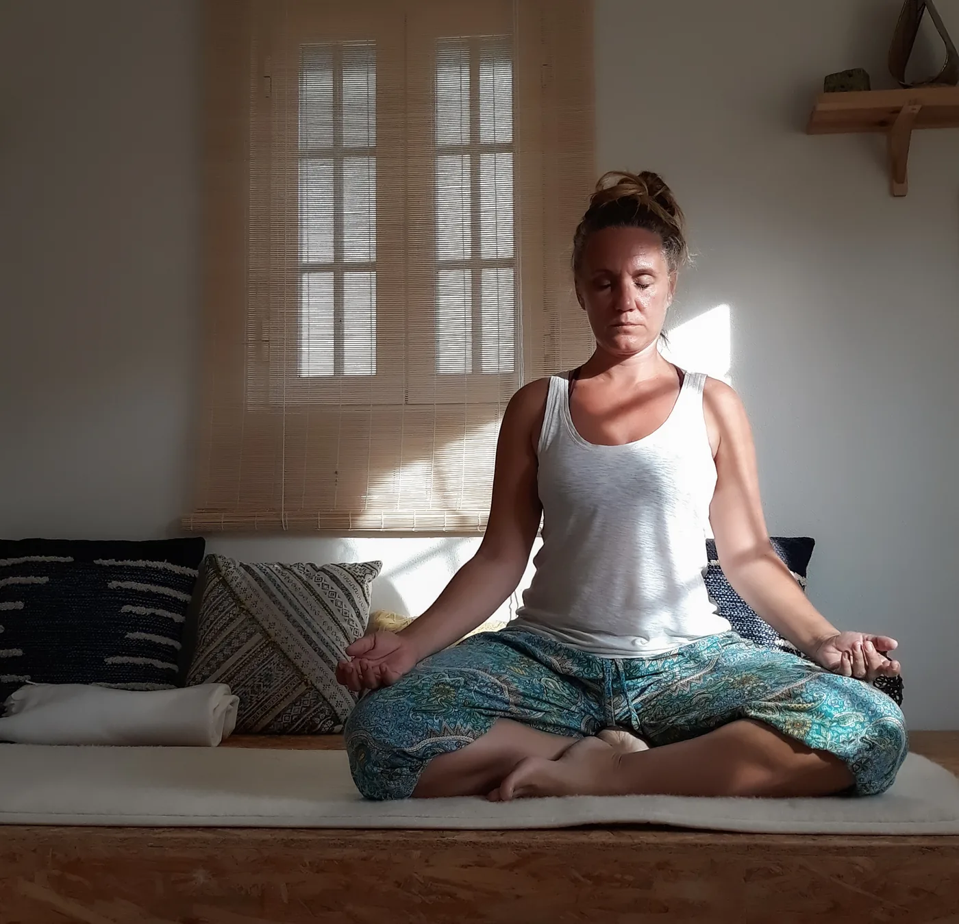 Patricia sentada em meditação na sala, de olhos fechados e com um mala na mão, à luz da janela.