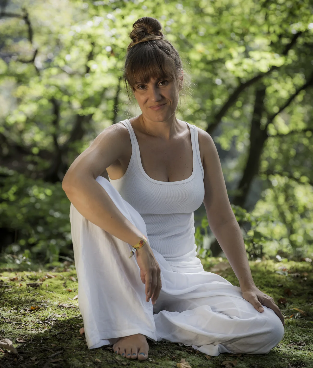 Patricia sentada no chão de um bosque, vestida de branco, a olhar para a câmara.