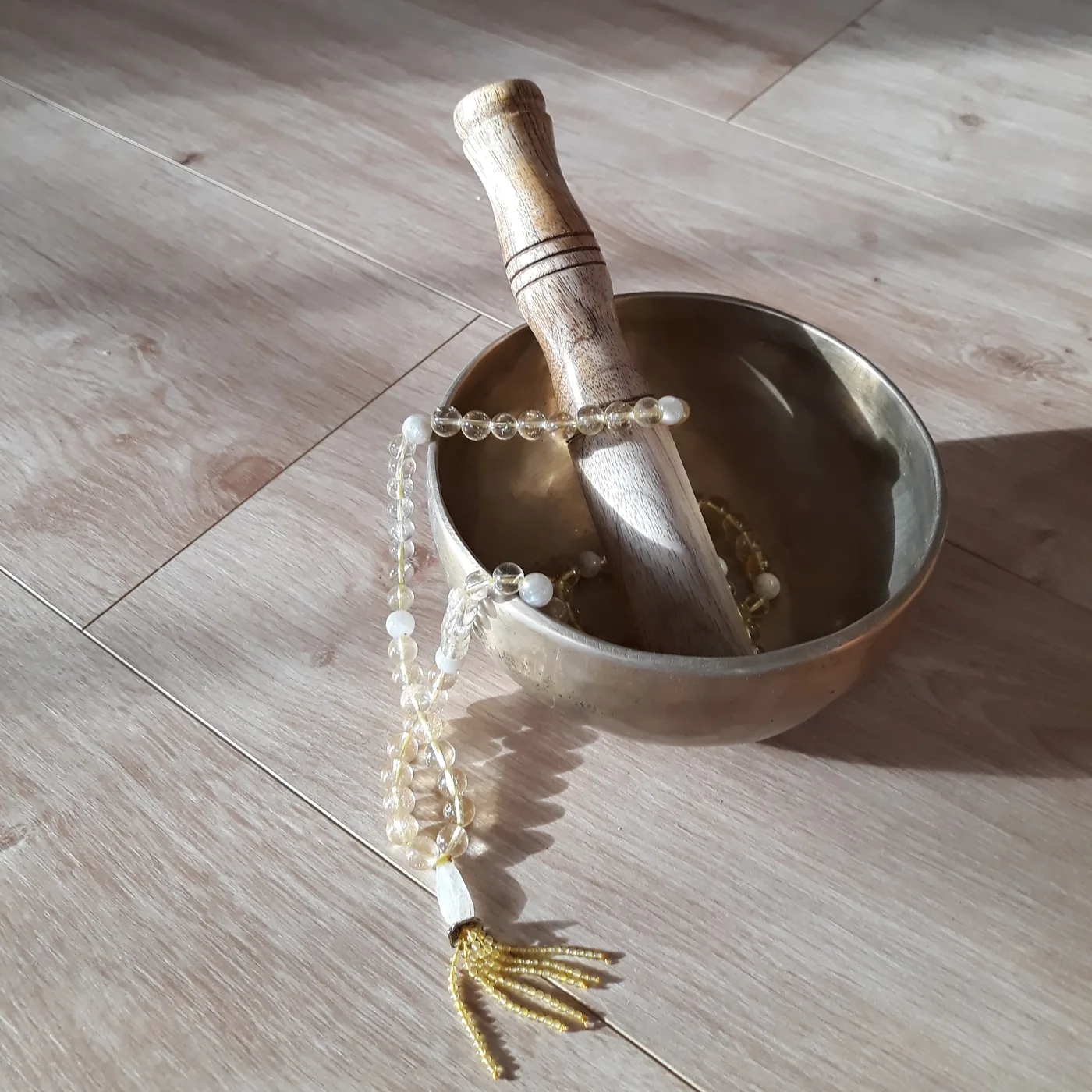 Taça tibetana com a sua maça de madeira e um mala de citrino, no chão de madeira da sala de yoga.