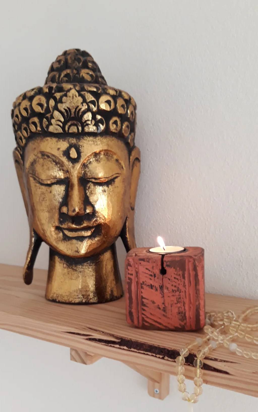 Cabeça de Buda dourada, uma vela acesa e um mala de citrino, na prateleira da sala de yoga.