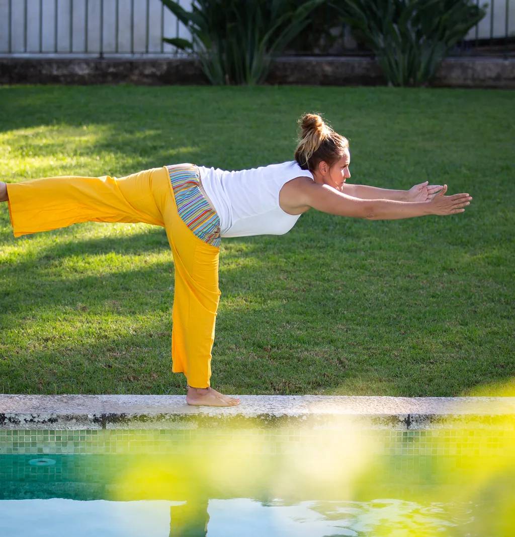 Patricia numa postura de equilíbrio, com uma perna estendida atrás e os braços à frente, junto à piscina da quinta.
