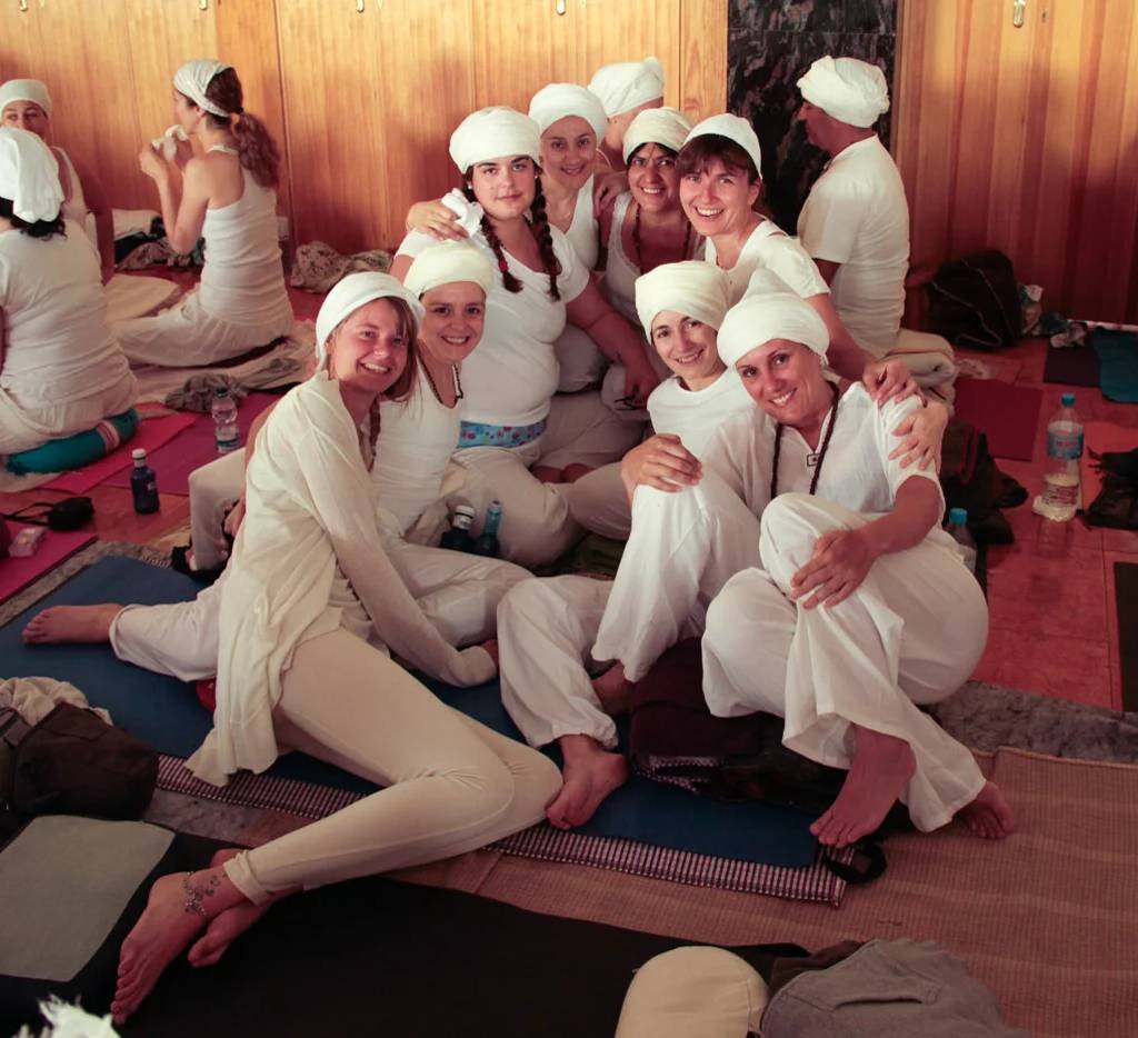 Grupo da formação de Kundalini Yoga, de branco e com turbante, sentado no chão a sorrir.