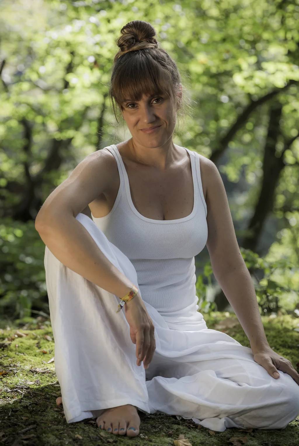 Patricia sentada no chão de um bosque, vestida de branco, a olhar para a câmara.