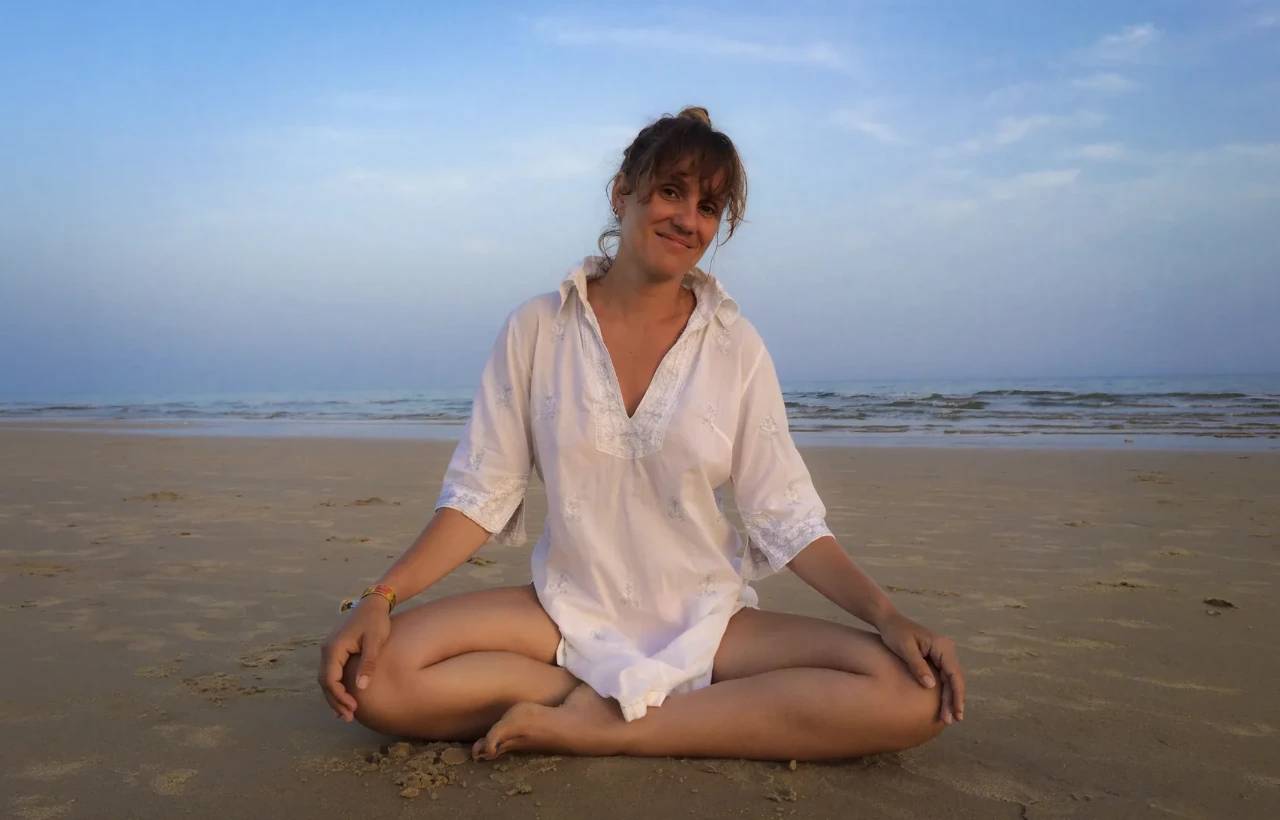Patricia sentada de pernas cruzadas na praia, ao fim do dia, a sorrir.