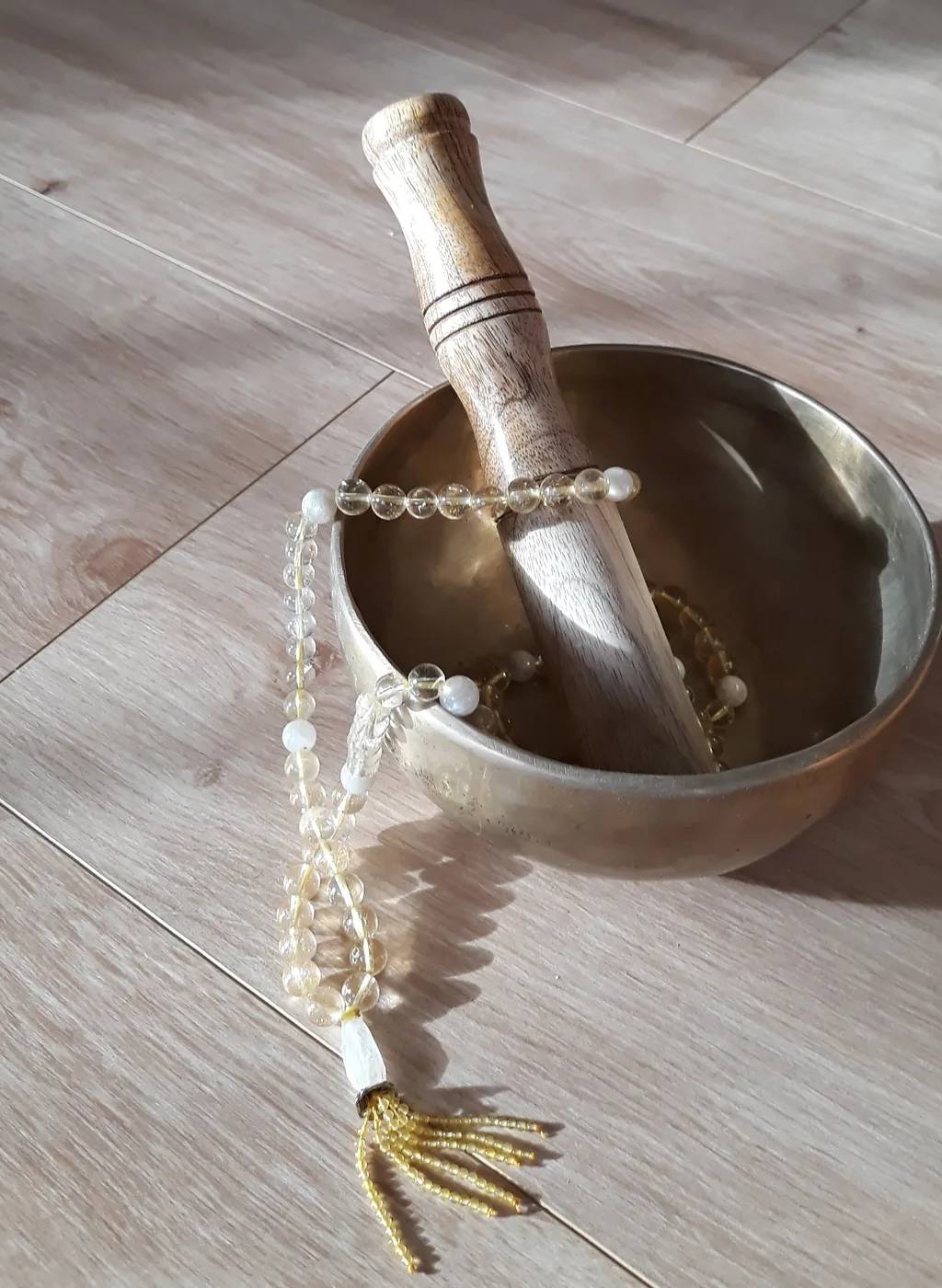 Taça tibetana com a sua maça de madeira e um mala de citrino, no chão de madeira da sala de yoga.